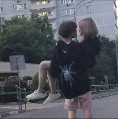 two people sitting on a skateboard in front of a building and one is holding the back of another person's head