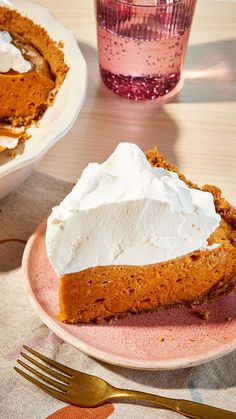 a slice of pumpkin pie on a pink plate next to a glass of water and fork