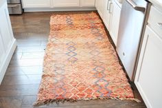 a kitchen with white cabinets and an orange rug on the floor next to the dishwasher