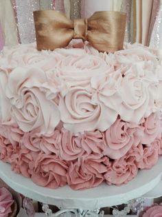 a cake with pink frosting and gold bows on top is sitting on a table