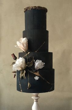 a three tiered black cake with white flowers on top