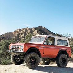 an orange truck driving down a dirt road next to a mountain covered in trees and bushes