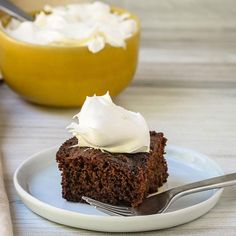 a piece of chocolate cake on a plate with a fork next to it and a bowl of whipped cream in the background