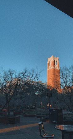 a clock tower is in the distance behind two chairs and tables on a sidewalk near trees