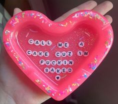 a hand holding a pink heart shaped cake tray with words written on the side and sprinkles all over it