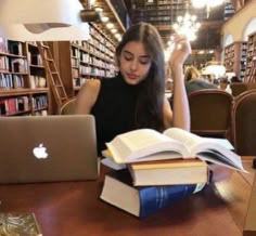 a woman sitting at a table in front of a laptop computer with books stacked on top of it