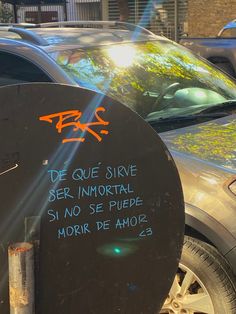 a parking meter with graffiti written on it next to parked cars in a city street