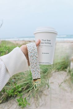 a person holding up a coffee cup in front of the beach