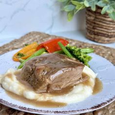 a white plate topped with meat covered in gravy next to veggies