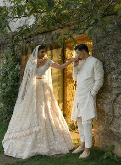 a bride and groom standing in front of a stone wall holding hands with each other