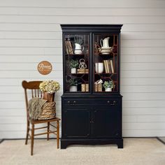 a black china cabinet sitting next to a wooden chair