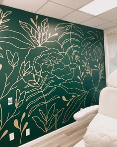 a white chair sitting in front of a green wall with gold flowers and leaves on it