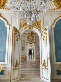 an ornate hallway with chandelier and chairs in the center is painted blue and gold