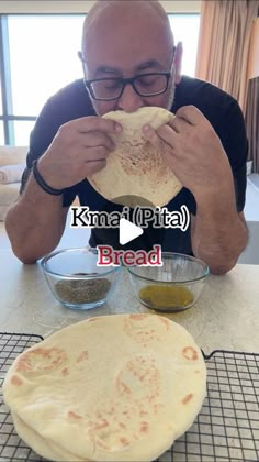 a man is eating bread with his hands and looking at the camera while sitting in front of an uncooked pita