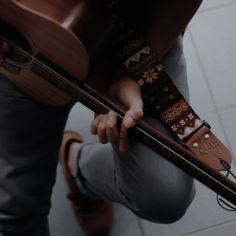 a person holding a guitar in their right hand and looking down at the ground with his left arm