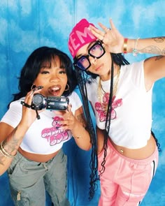 two young women posing for a photo with one holding a camera and the other taking a selfie