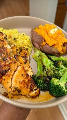 a person holding a plate with chicken, broccoli and mashed potatoes