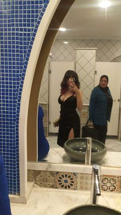 a woman taking a selfie in front of a bathroom mirror with blue tiles on the walls