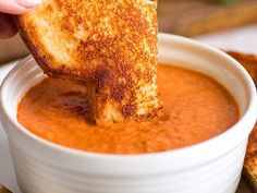 a grilled cheese sandwich being dipped into a bowl of tomato soup with toast on the side