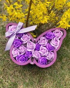 a purple butterfly shaped box with roses in it sitting on the ground next to yellow flowers