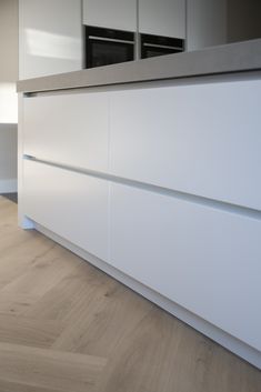 an empty kitchen with white cabinets and wood flooring