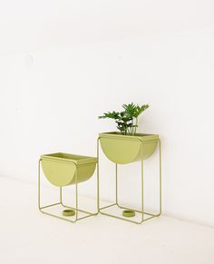 two green planters sitting next to each other on top of a white floor with a wall in the background