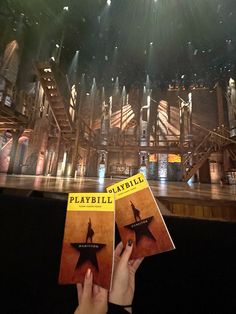 two people are holding up their books in front of a stage with lights on it