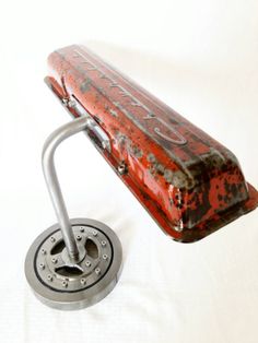 an old red suitcase sitting on top of a metal stand next to a white background