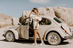 a woman standing next to an old car in the desert with her hand on her head