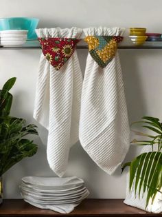 two white towels hanging on a shelf next to plates and bowls with plants in the background