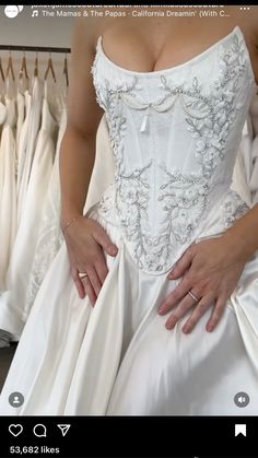 a woman in a white wedding dress with her hands on her hips, standing next to some dresses