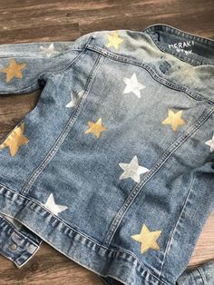 a denim jacket with gold stars on the front and back, sitting on top of a wooden