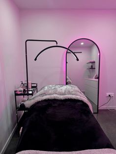 a room with a bed, mirror and lights in the corner is lit up by pink lighting