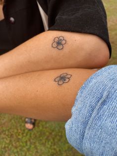 two people with tattoos on their legs sitting next to each other in the grass and one is holding a cell phone