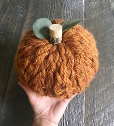 a hand is holding an orange yarn ball with a green leaf on the top and bottom