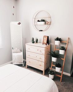 a bedroom with a dresser, mirror and potted plants on the shelf next to it