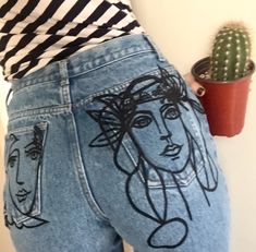 a woman wearing high waisted jeans with drawings on her butts and holding a cactus