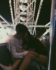 a man and woman sitting next to each other in front of a ferris wheel at night