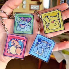 four different colored pokemon keychains are held in someone's hand