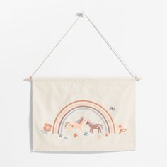 a white wall hanging with horses and rainbows in the background on a wooden hanger