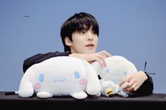 a young man holding two stuffed animals on top of a black cloth covered table next to a blue wall