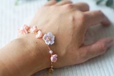 a woman's hand holding a bracelet with pink flowers and white pearls on it