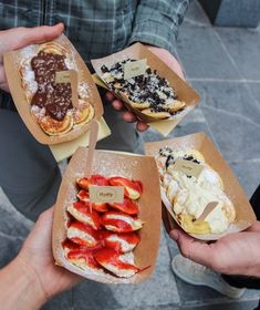 four people are holding small sandwiches with toppings in paper containers on the ground,