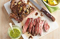 sliced steak on cutting board next to bowl of fruit and knife with green sauce in glass container