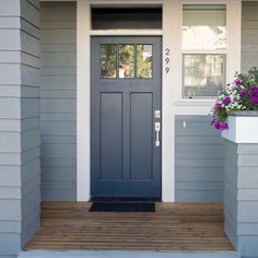 a blue front door on a gray house with purple flowers in the window and white trim