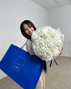 a woman holding a blue shopping bag with white flowers in it's hand and smiling at the camera