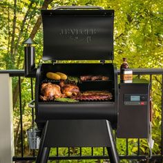 a bbq grill with meat and vegetables cooking on the outside deck overlooking some trees