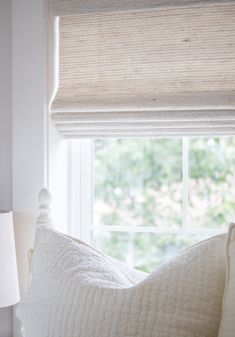 a white bed sitting under a window next to a lamp