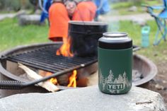 a yeti can sitting next to an open fire pit with people in the background