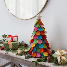 a colorful christmas tree sitting on top of a table next to presents and a mirror